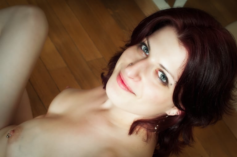 Close-up of a smiling woman with auburn hair, lying on a wooden floor. An intimate and bright boudoir photo highlighting her captivating gaze.