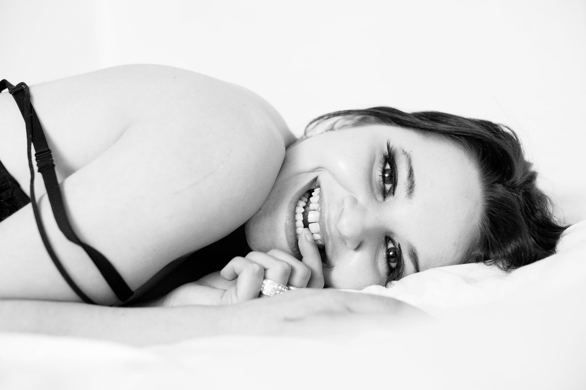 Smiling woman lying on a bed during a boudoir photo session in black and white.